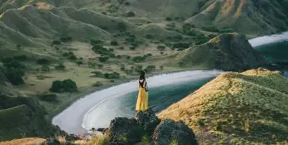 person standing on mountain near other mountains and water
