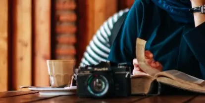 person sitting at table with camera and drink reading book