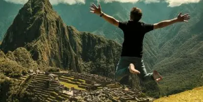 person jumping in front of green mountain and ruins