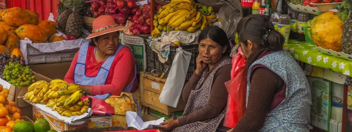 three people sitting surrounded by colorful fruits at an outdoor market