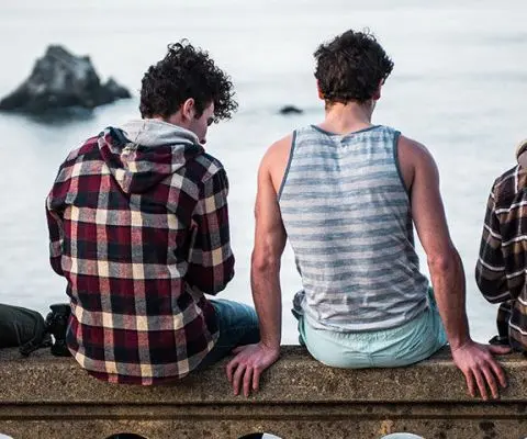 four people sitting and facing the ocean