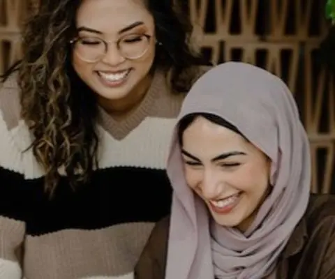 two smiling people looking at tablet device while one sits and the other stands
