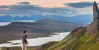 person standing on rock looking at larger rock formations surrounded by green grass