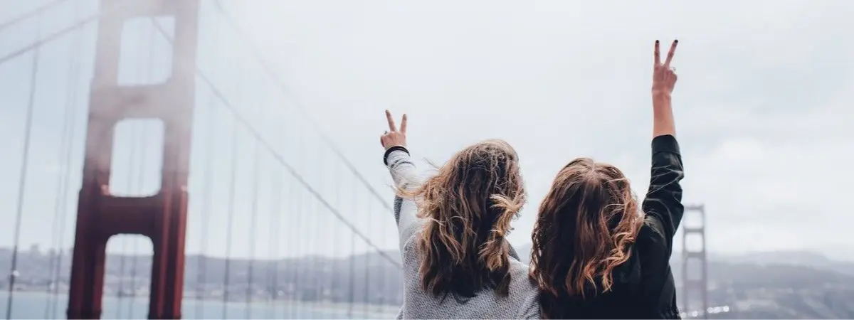 two people making peace signs near red bridge and fog