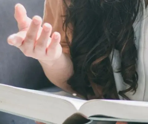 person sitting on couch with open book gesturing with one hand