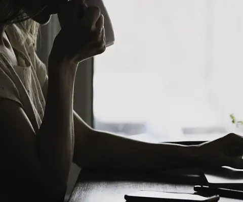 woman in shadow sipping coffee working on laptop 