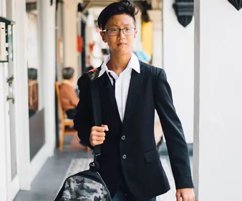 young man in white button up and black blazer with duffle bag over his shoulder