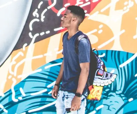 young black man dressed fashionably in front of large, brightly colored mural