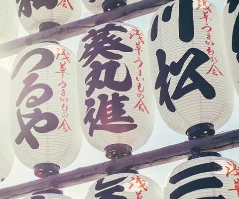 rows of white lanterns with black and red japanese characters on them.