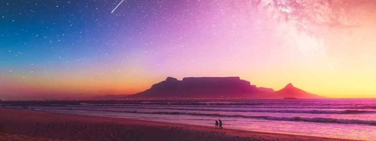 people standing on beach with mountain in the background under colorful night sky