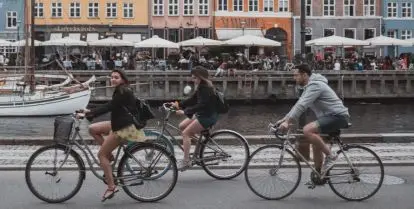 three people on bicycles in front of water and colorful buildings