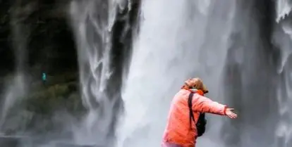 person with arms outstretched standing in front of waterfall